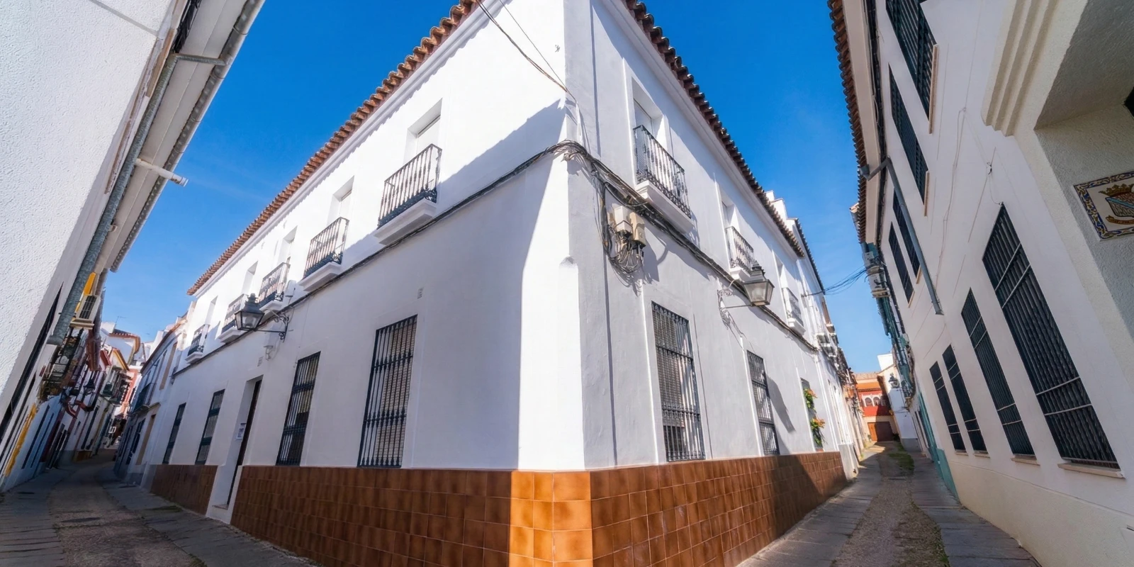 Edificio blanco de esquina con cielo azul y calles estrechas a ambos lados.