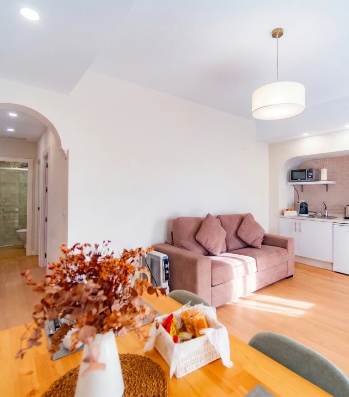 Sala moderna con sof&aacute;, cocina compacta y mesa de comedor; decoraci&oacute;n c&aacute;lida y luminosa.