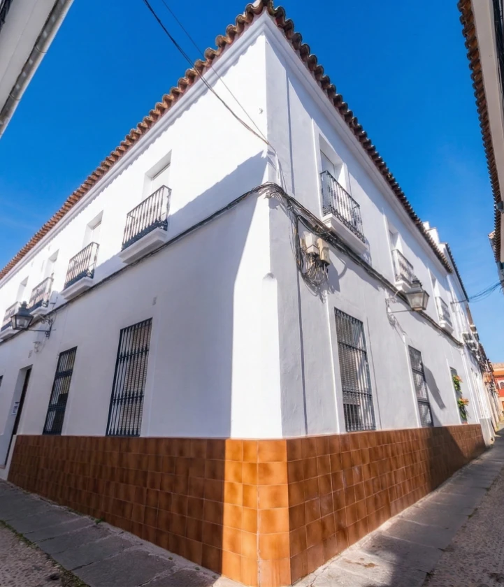 Esquina de edificio blanco con base marr&oacute;n bajo cielo azul.