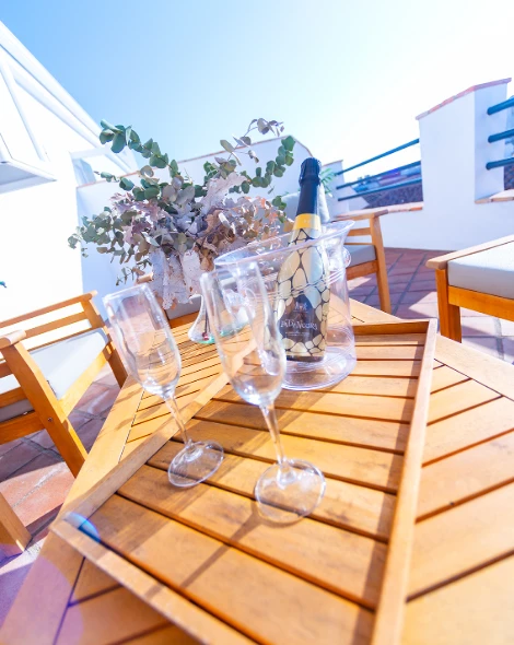 Mesa al aire libre con copas, botella de champ&aacute;n en hielera, y flores secas.