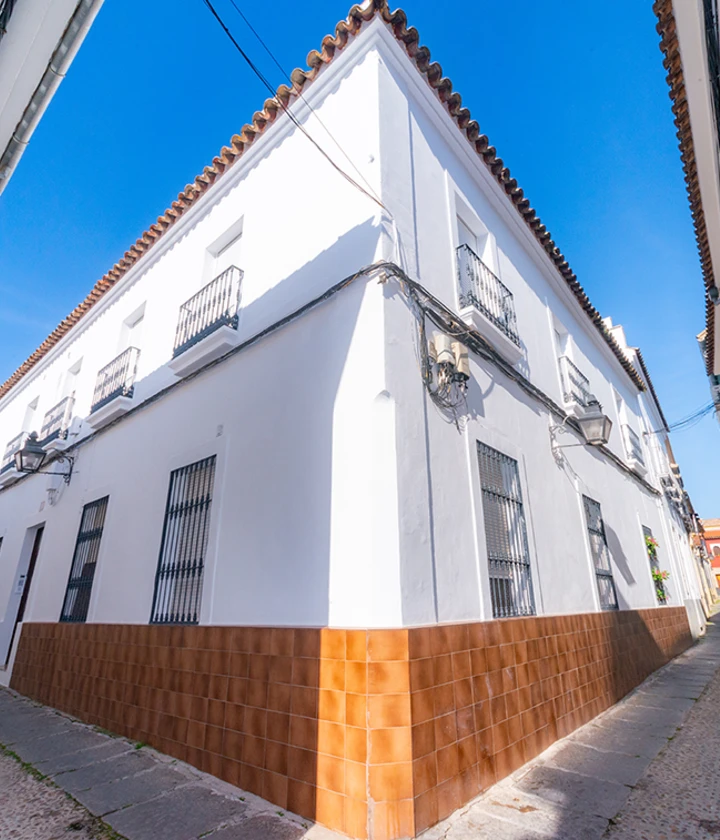 Edificio blanco de esquina con azulejos marrones y ventanas enrejadas, bajo un cielo azul.
