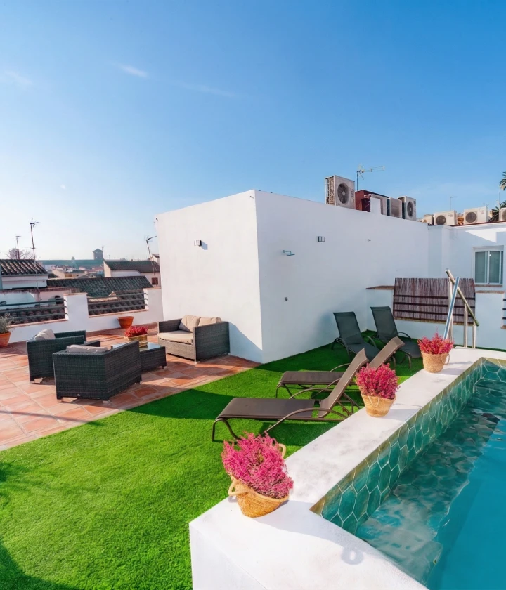 Azotea con piscina, c&eacute;sped artificial, tumbonas, y muebles de mimbre bajo un cielo despejado.