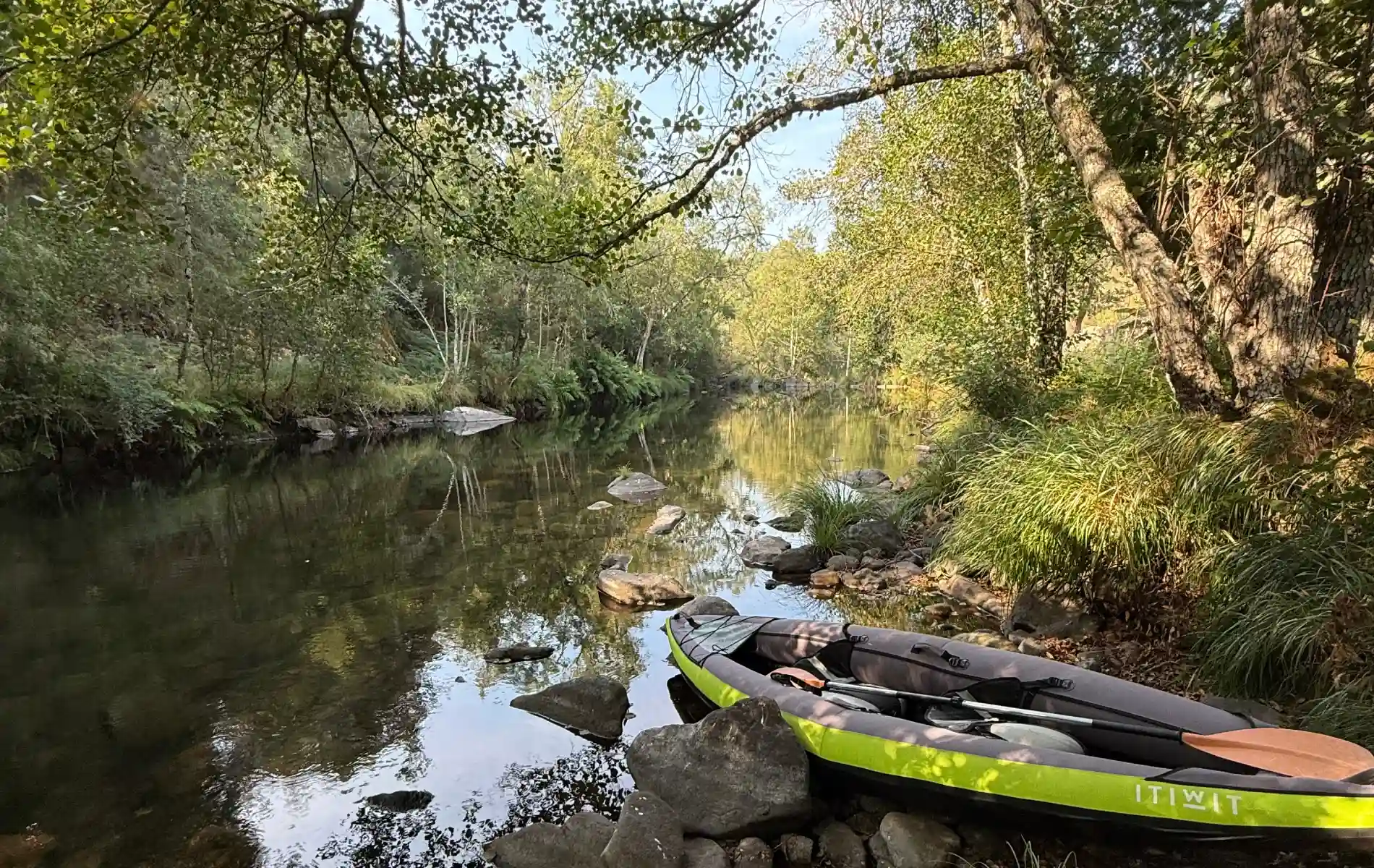 Caiaque verde em margem de rio cercado por &aacute;rvores.