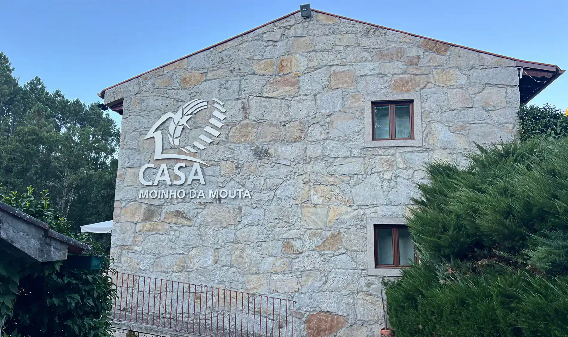 Casa de pedra com logo "Casa Moinho da Mouta" na fachada.