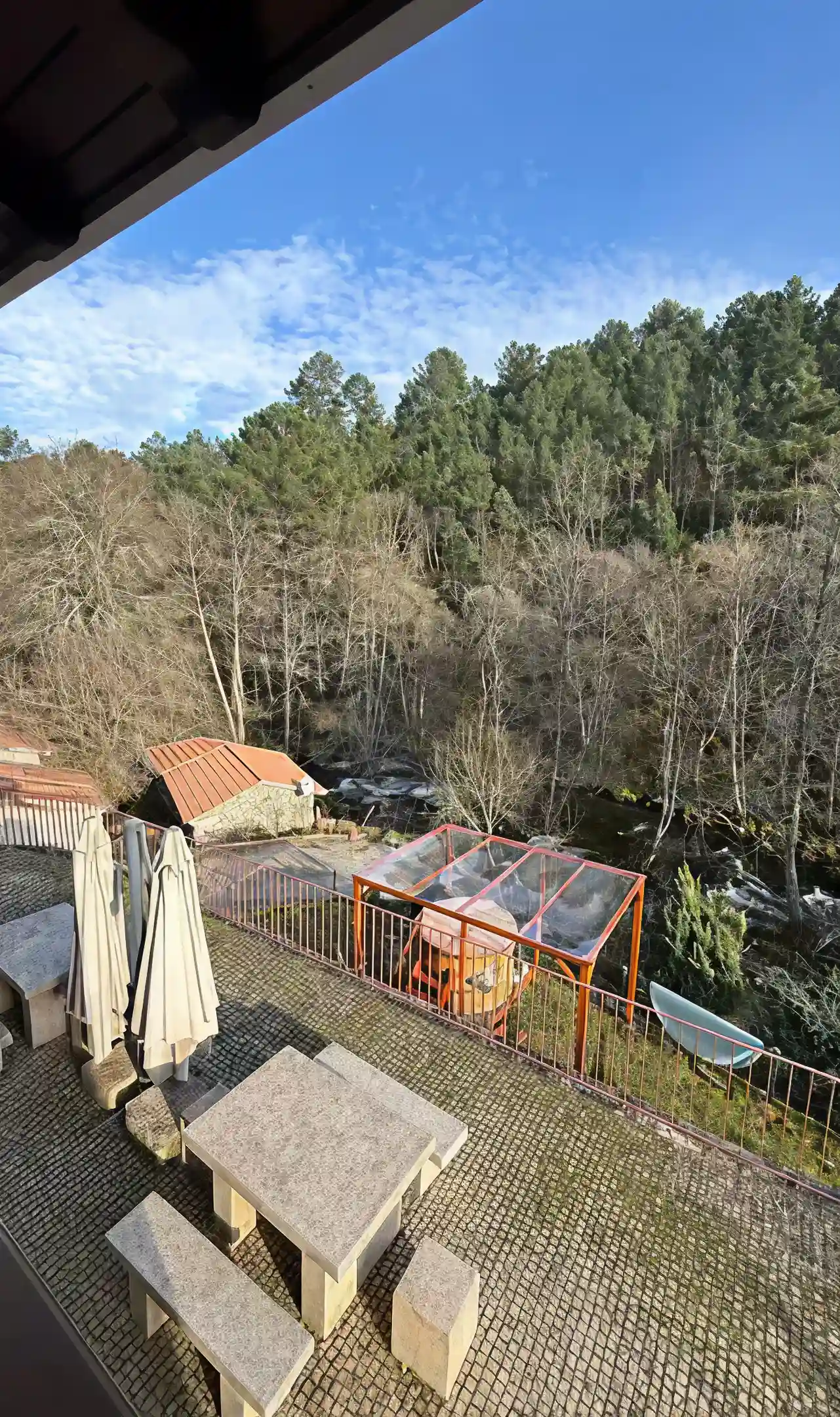 Terra&ccedil;o com mesas de pedra, guarda-s&oacute;is e floresta ao fundo.
