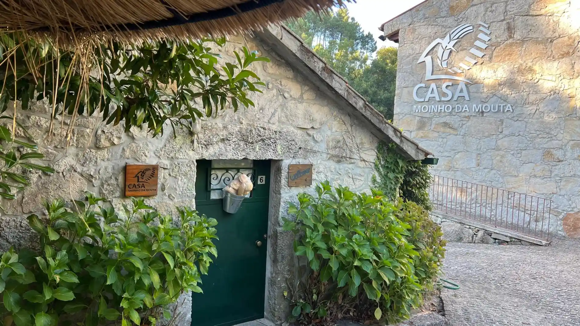Casa de pedra com vegeta&ccedil;&atilde;o e placa: "Casa Moinho da Mouta".
