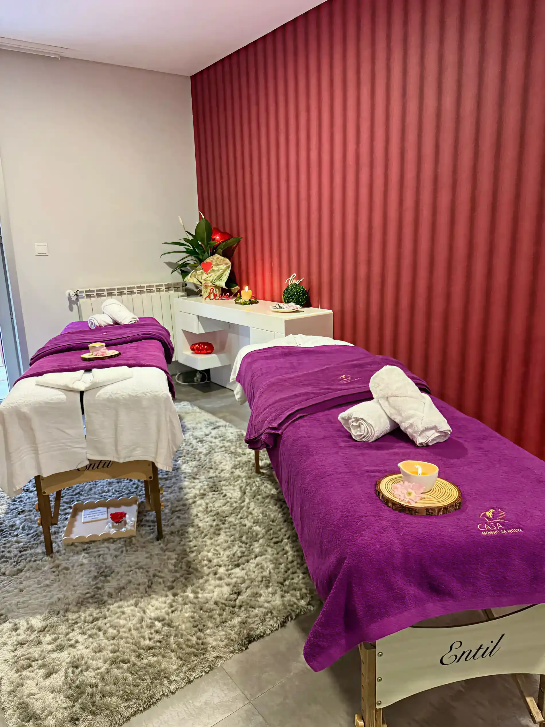 Sala de massagem com duas macas cobertas por toalhas roxas e velas acesas.