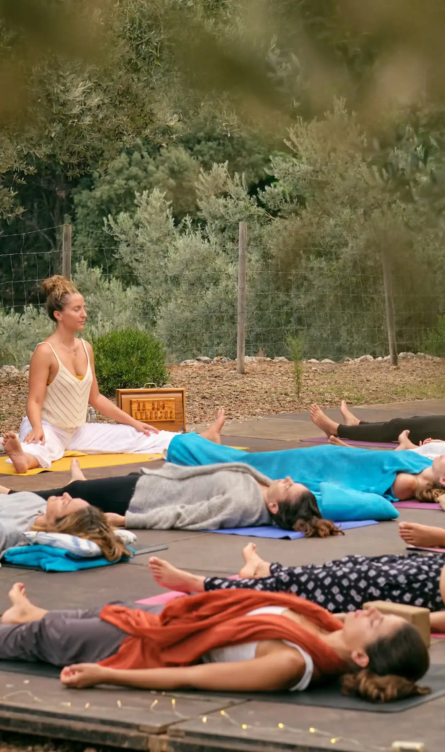 Grupo praticando yoga ao ar livre sob &aacute;rvores.