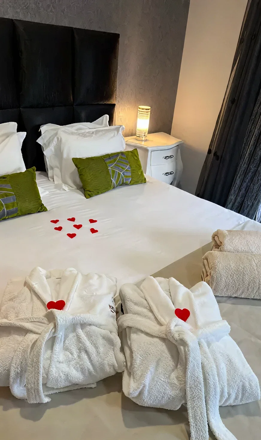 Cama com roup&otilde;es e cora&ccedil;&otilde;es decorativos sobre len&ccedil;&oacute;is brancos.