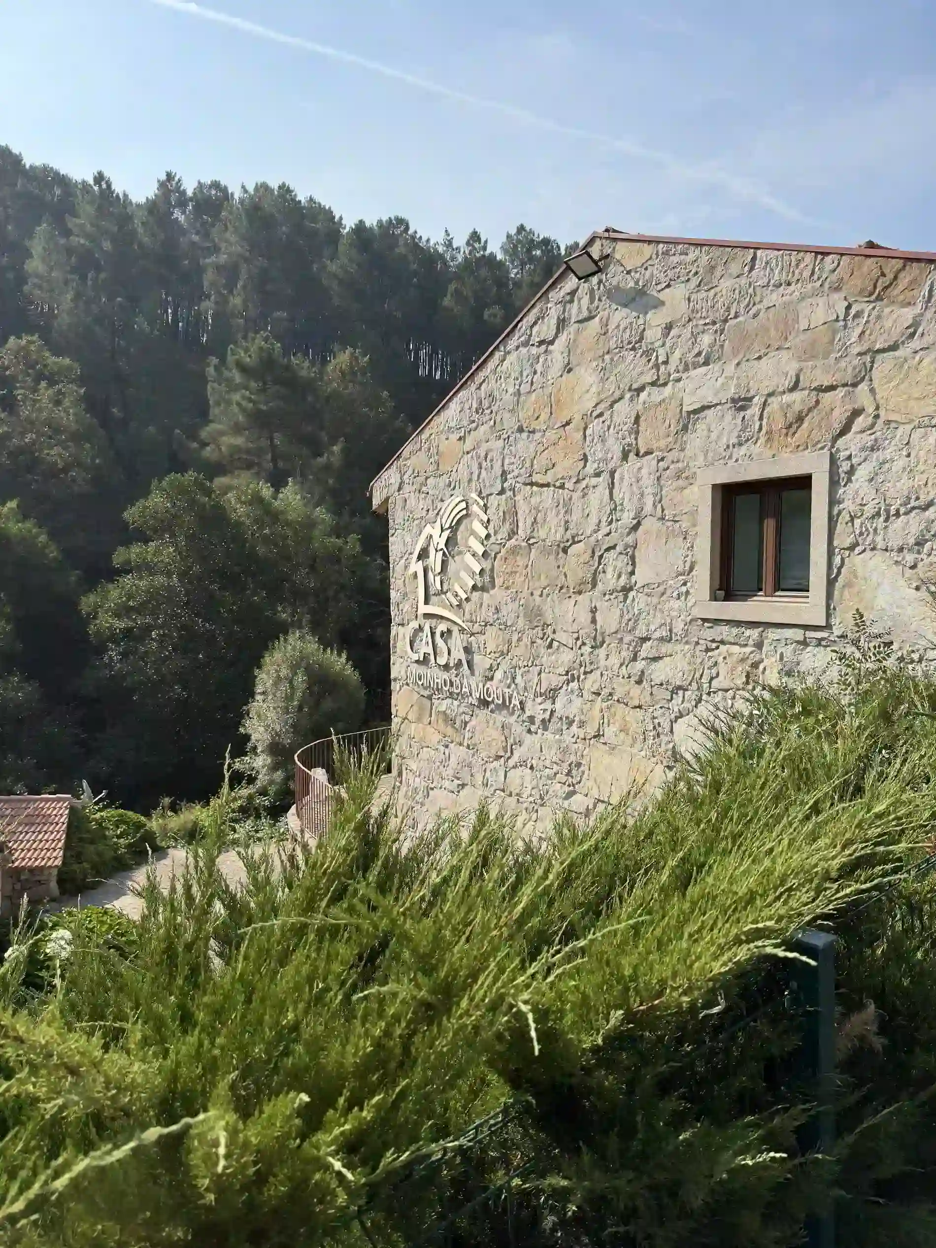 Casa de pedra em meio &agrave; natureza, rodeada por &aacute;rvores e arbustos verdes.
