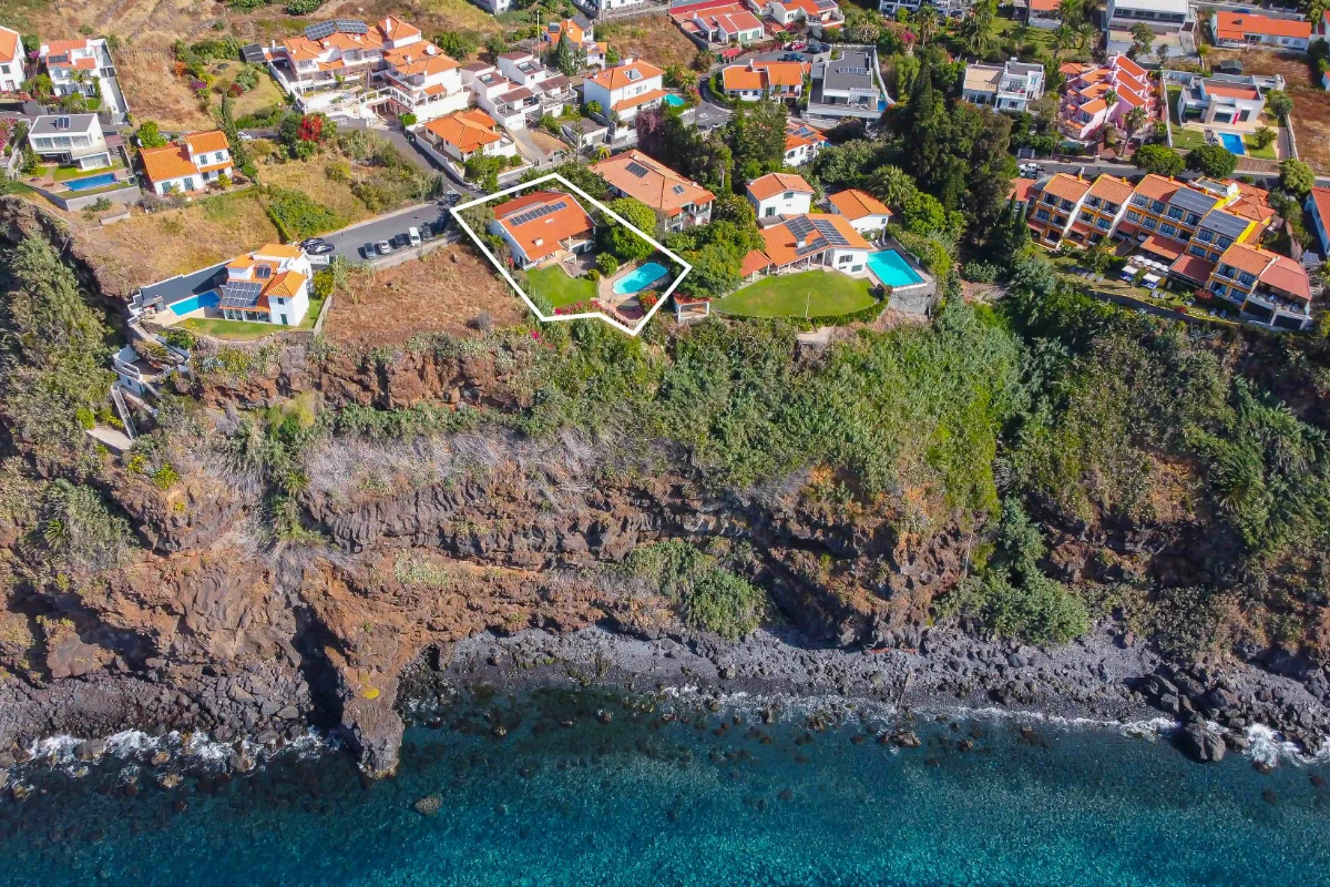 Vista aérea de casas en un acantilado junto al mar con agua turquesa.