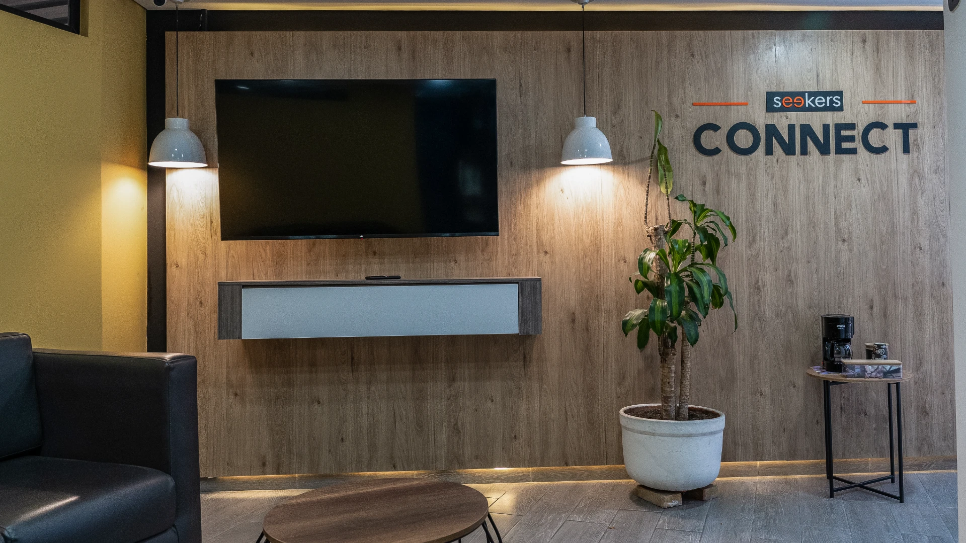 Sala de espera moderna con TV, planta, mesa y l&aacute;mparas.