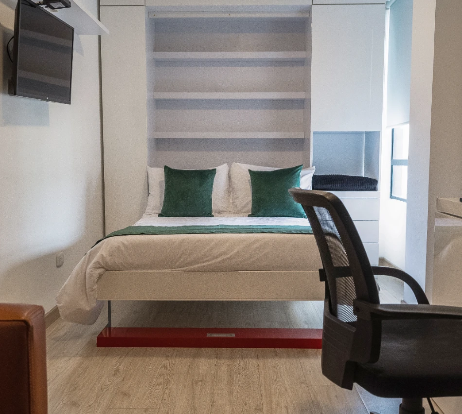 Cama con almohadas verdes en una habitaci&oacute;n moderna con silla y televisor.