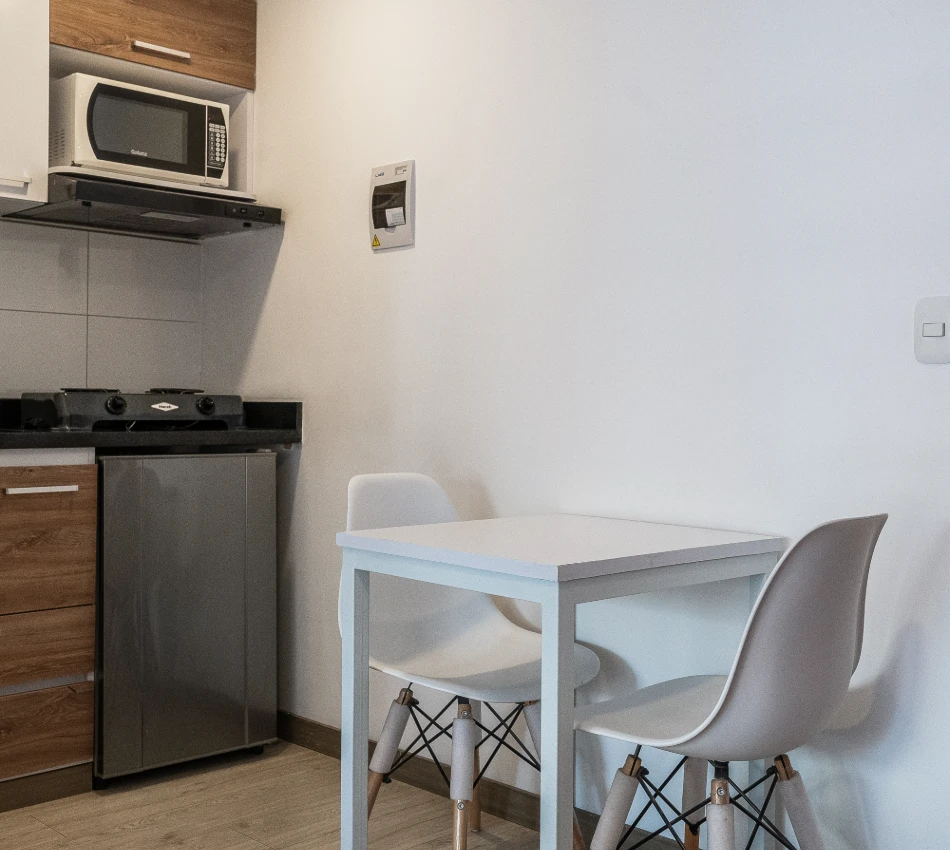 Peque&ntilde;a cocina con mesa y sillas blancas, microondas y estufa.