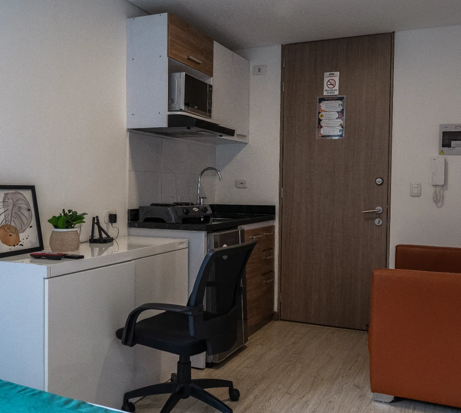 Peque&ntilde;a cocina con escritorio, silla, y sof&aacute; en un apartamento.