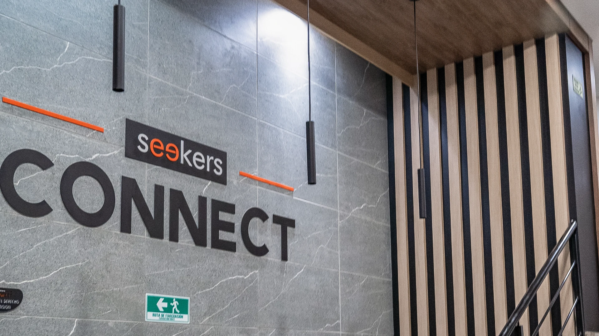Muro gris con el texto "Seekers Connect" y se&ntilde;al de evacuaci&oacute;n abajo.