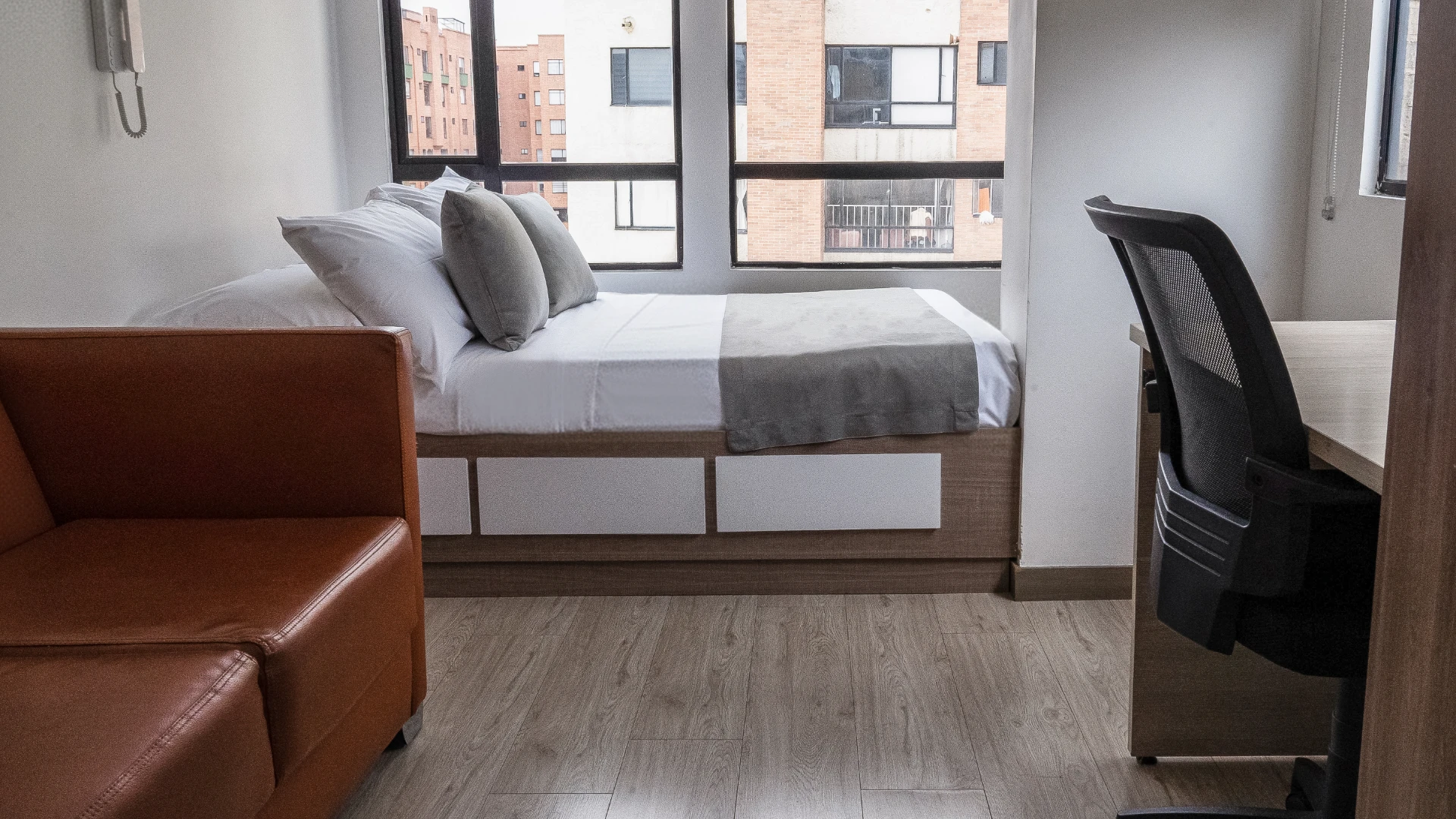 Habitaci&oacute;n peque&ntilde;a con cama, sof&aacute; de cuero y escritorio junto a la ventana.