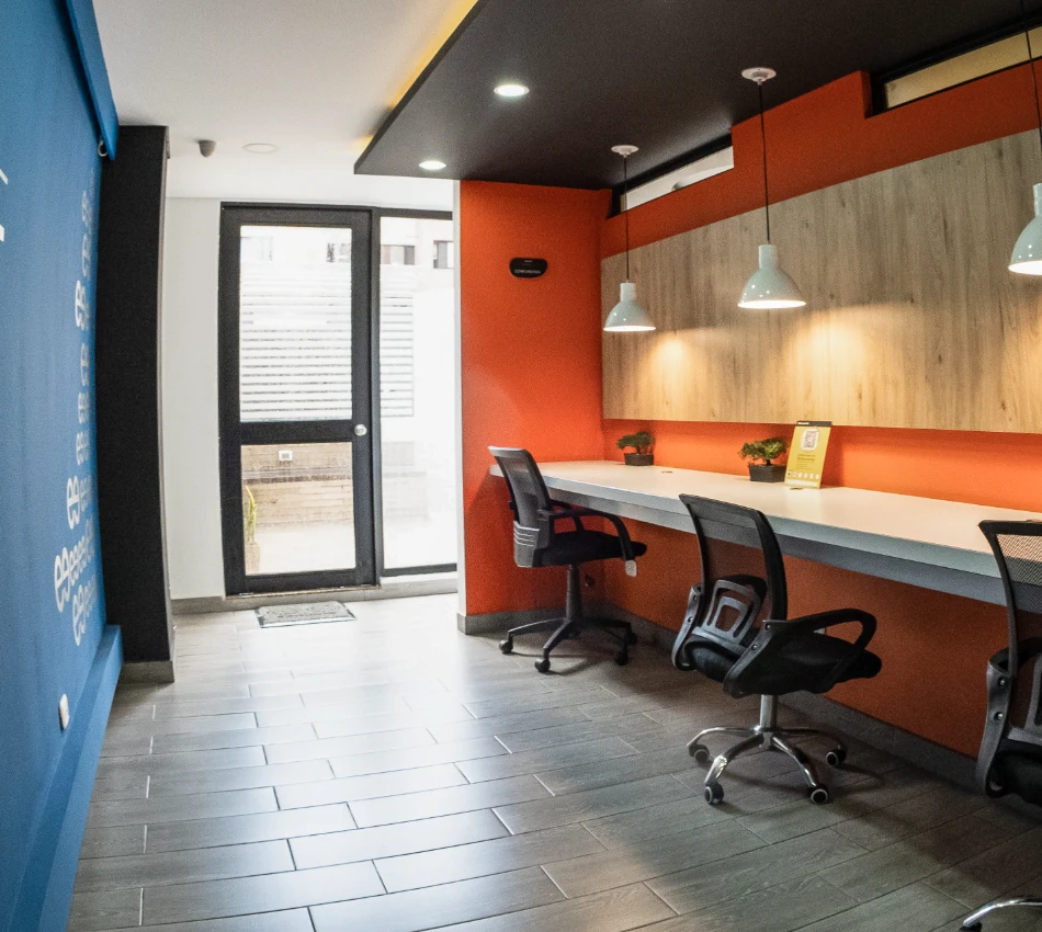 Oficina moderna con paredes naranjas y azules, sillas y l&aacute;mparas colgantes.