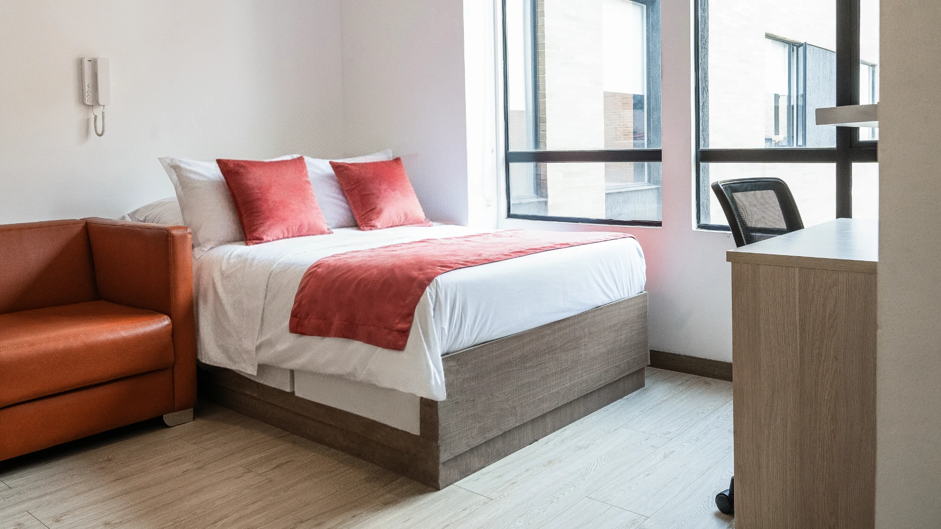 Habitaci&oacute;n moderna con cama, sof&aacute;, escritorio y ventanas grandes.