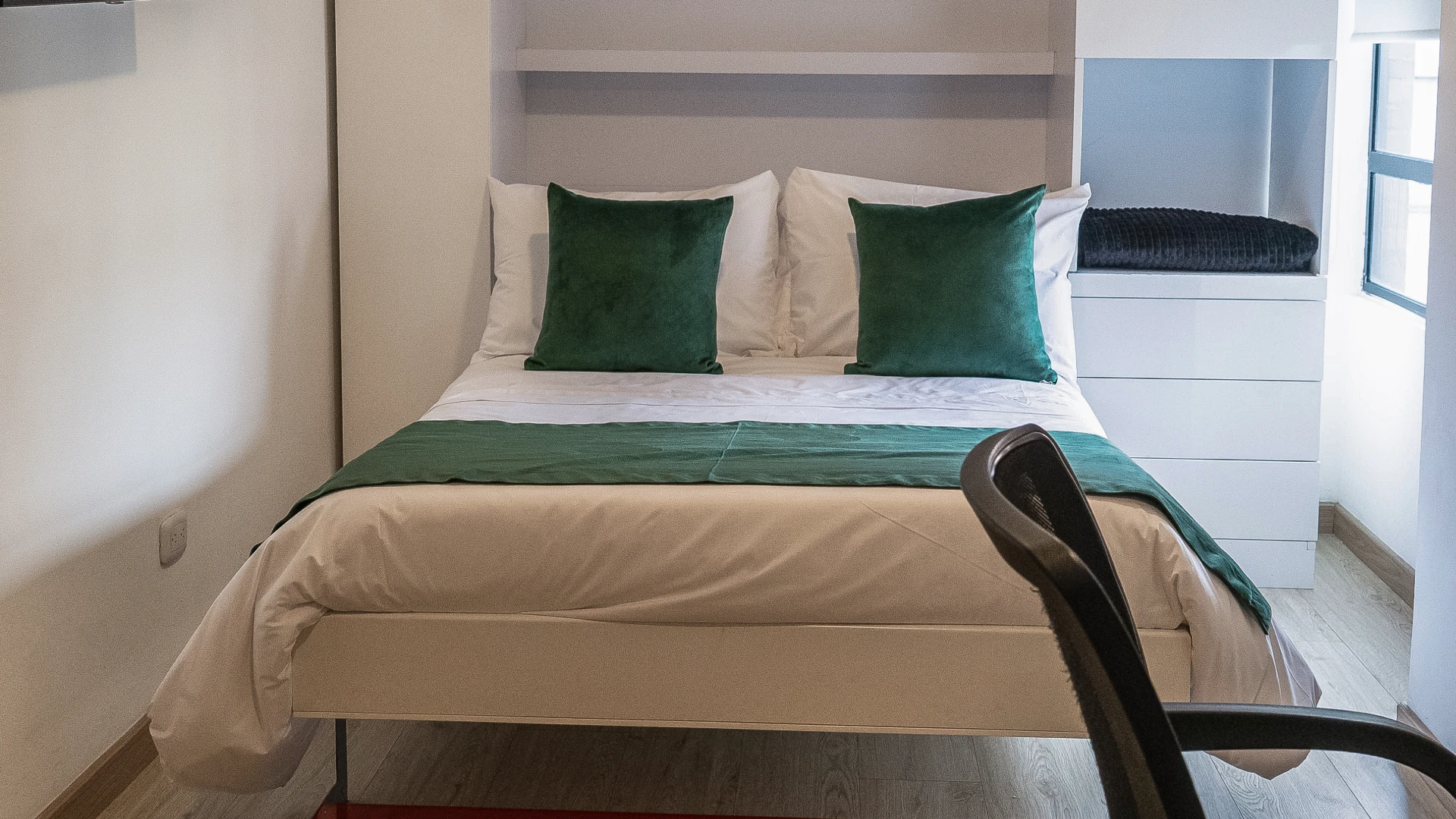 Habitaci&oacute;n con cama doble, cojines verdes y silla de oficina negra.