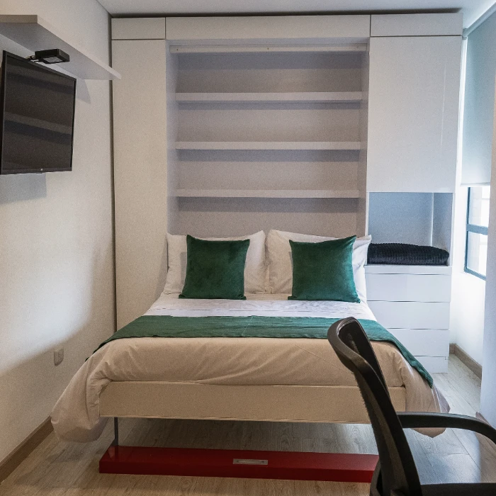 Habitaci&oacute;n moderna con cama, TV y estanter&iacute;a, decorada en blanco y verde.