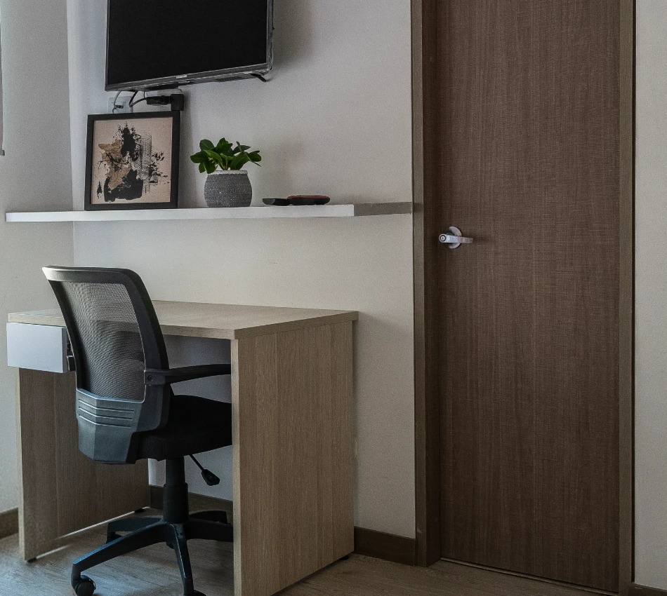 Escritorio y silla negra junto a puerta marr&oacute;n y estante con planta y cuadro.