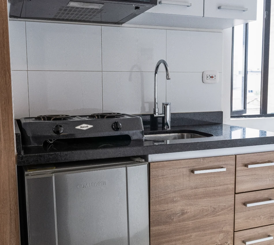 Cocina moderna con estufa de gas, fregadero y nevera peque&ntilde;a.