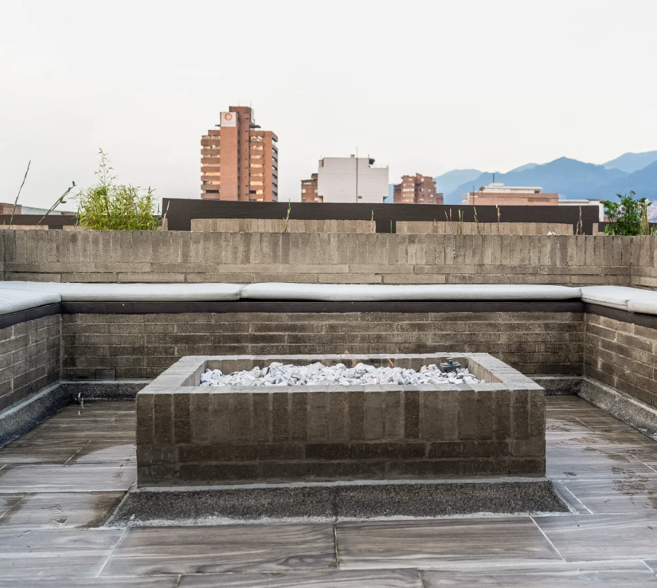 Terraza con fogata de piedra y vistas a edificios y monta&ntilde;as al fondo.