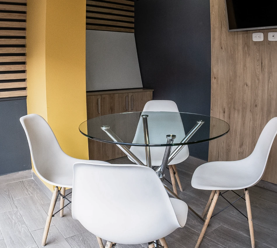 Mesa redonda de cristal rodeada de sillas blancas en una sala moderna.