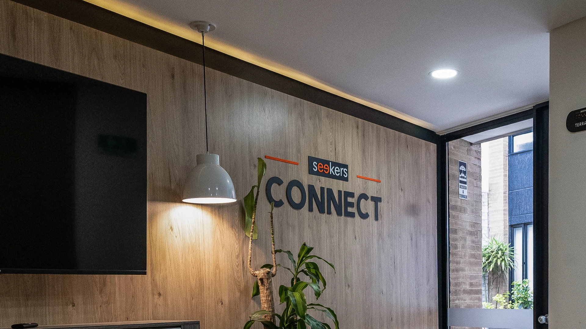 Pared con el logo "Seekers Connect", planta y l&aacute;mpara colgante blanca.