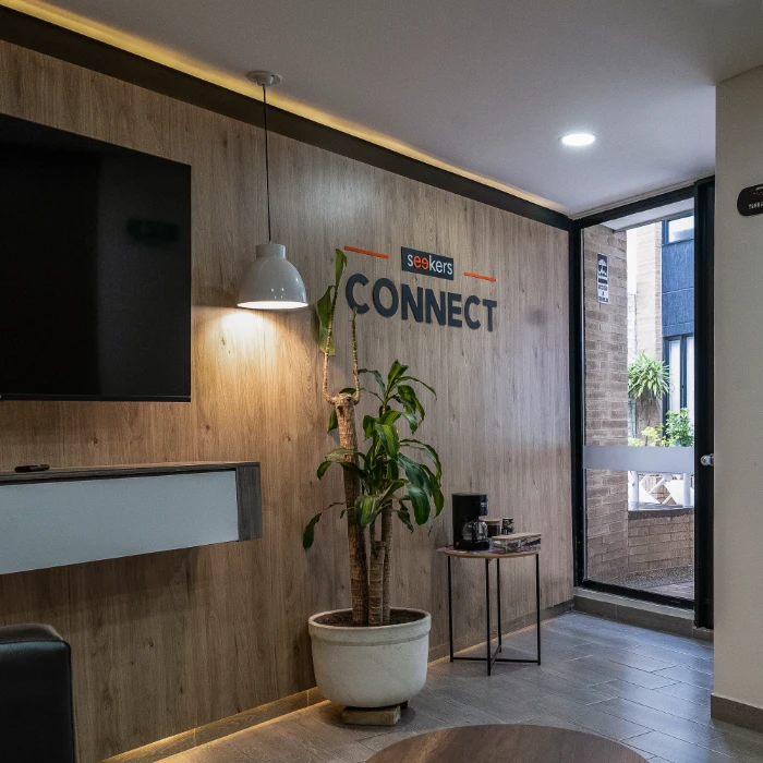 Sala moderna con planta, l&aacute;mpara y letras "seekers CONNECT" en la pared.