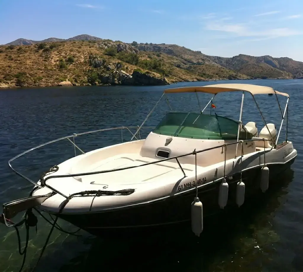 Lancha blanca anclada en el agua cerca de la costa rocosa.