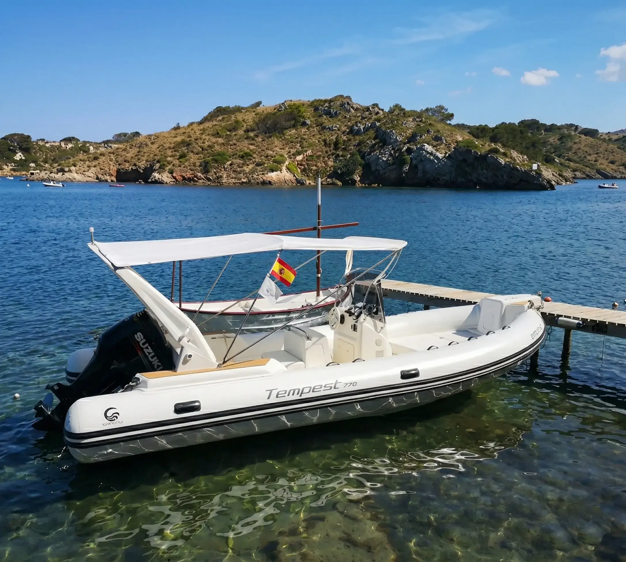 Lancha blanca amarrada en un muelle sobre agua cristalina, isla al fondo.