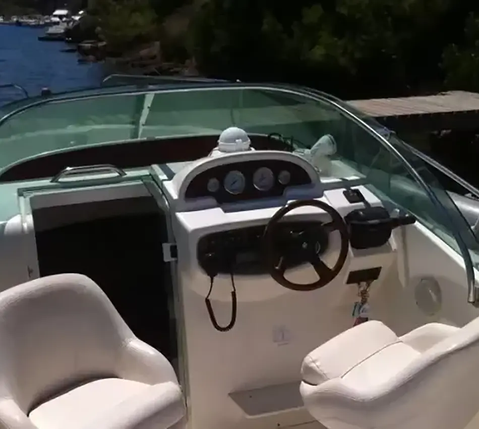Interior de un bote con volante y asientos blancos frente al agua.