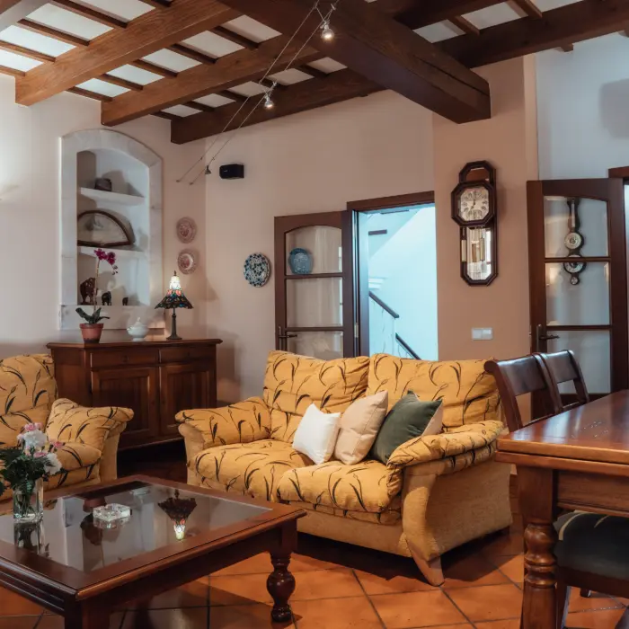 Sala acogedora con techo de madera, sof&aacute; amarillo y decoraci&oacute;n tradicional.