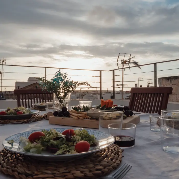 Mesa al aire libre con platos de ensalada al atardecer en una azotea.
