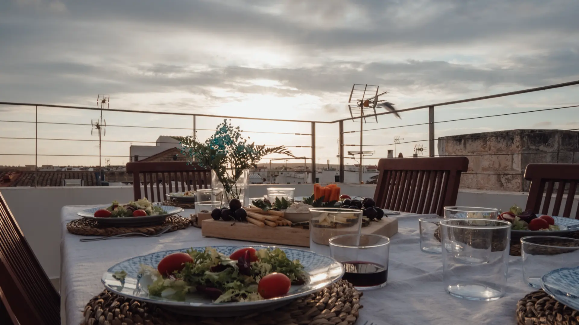 Mesa servida al aire libre con ensaladas y copas al atardecer.