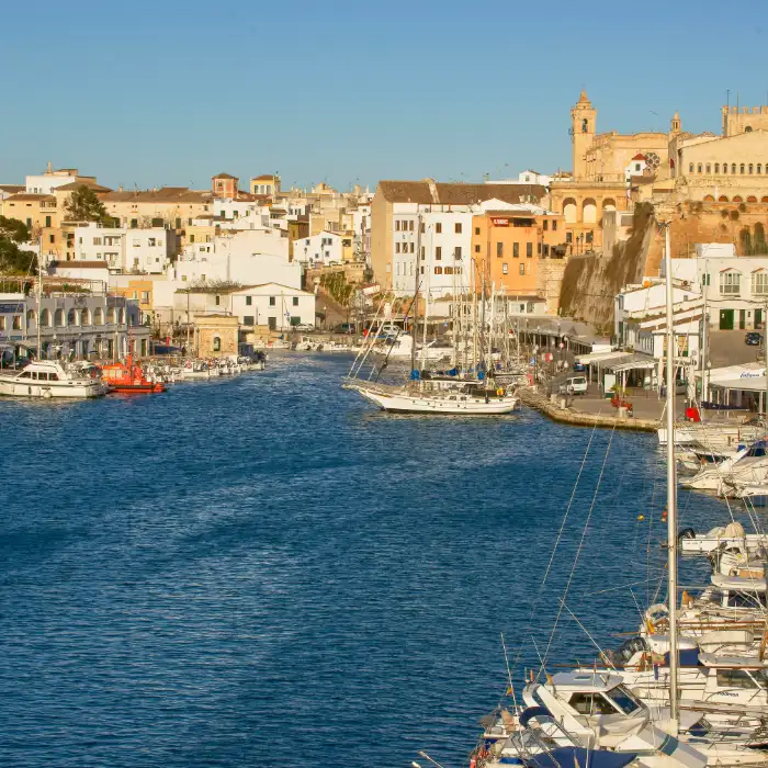 Puerto con barcos y edificios hist&oacute;ricos al fondo bajo un cielo despejado.