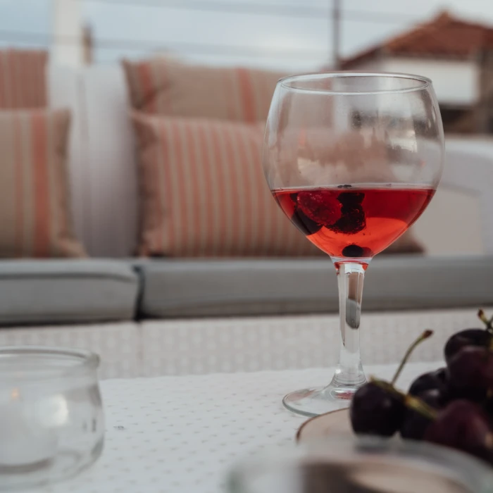 Copa de bebida rosada con frutas sobre una mesa, sill&oacute;n al fondo.