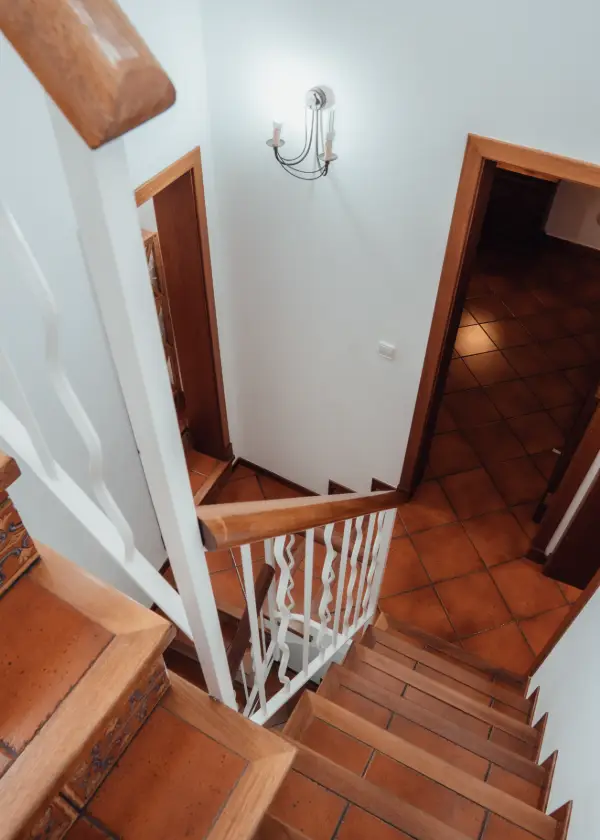 Escalera de madera con baranda blanca en un interior iluminado.