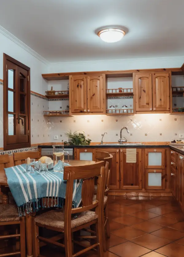 Cocina r&uacute;stica con muebles de madera y mesa cubierta por mantel azul.