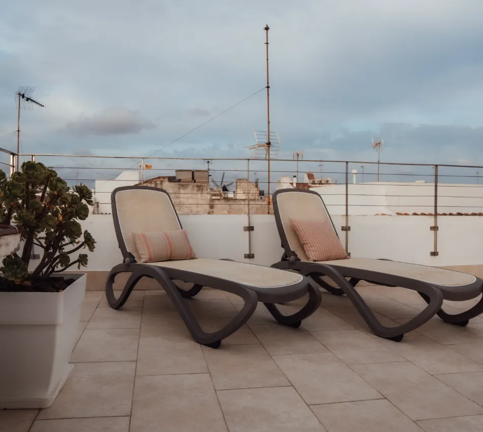 Dos tumbonas con cojines en una terraza con cielo nublado.