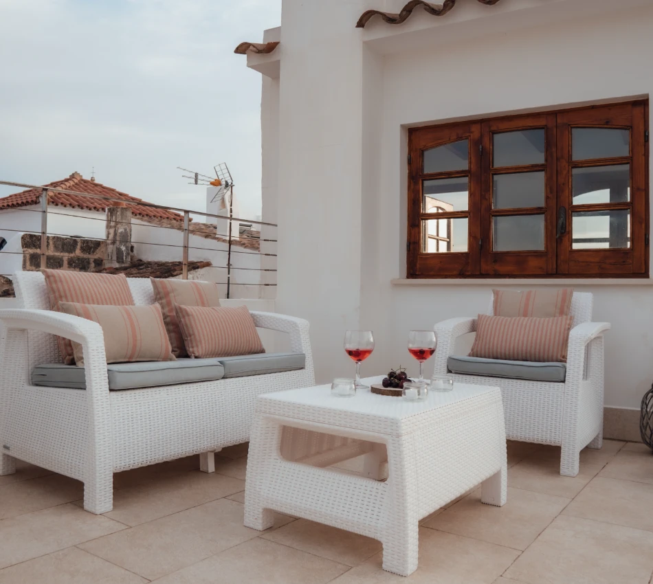 Terraza con sillones blancos, mesa con copas de vino y ventanas de madera.