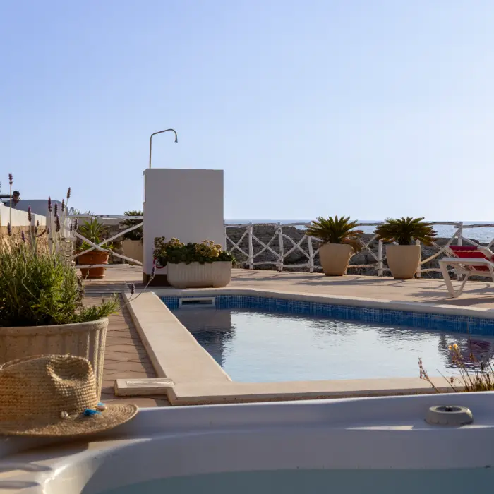 Piscina al aire libre con plantas y sombrero de paja al borde del agua.