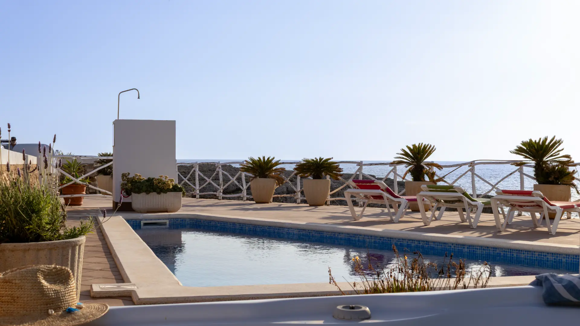 Piscina con tumbonas y plantas junto al mar en un d&iacute;a soleado.