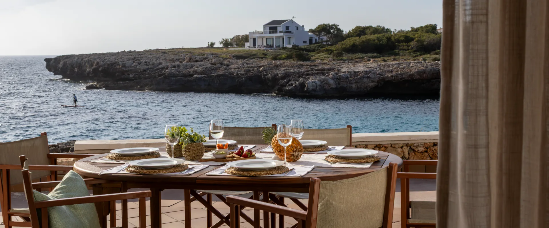 Mesa al aire libre con vista al mar y una casa blanca en la distancia.