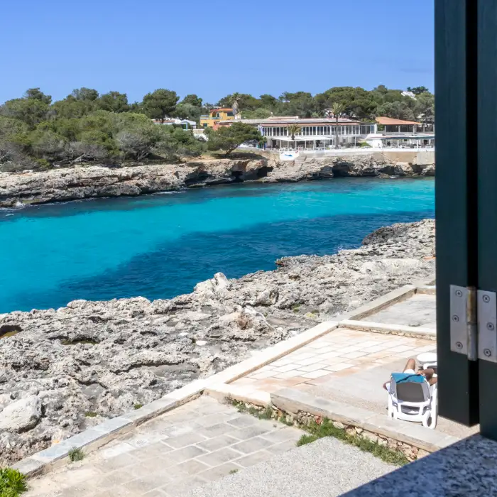Vista de una costa rocosa con mar turquesa y edificios al fondo.