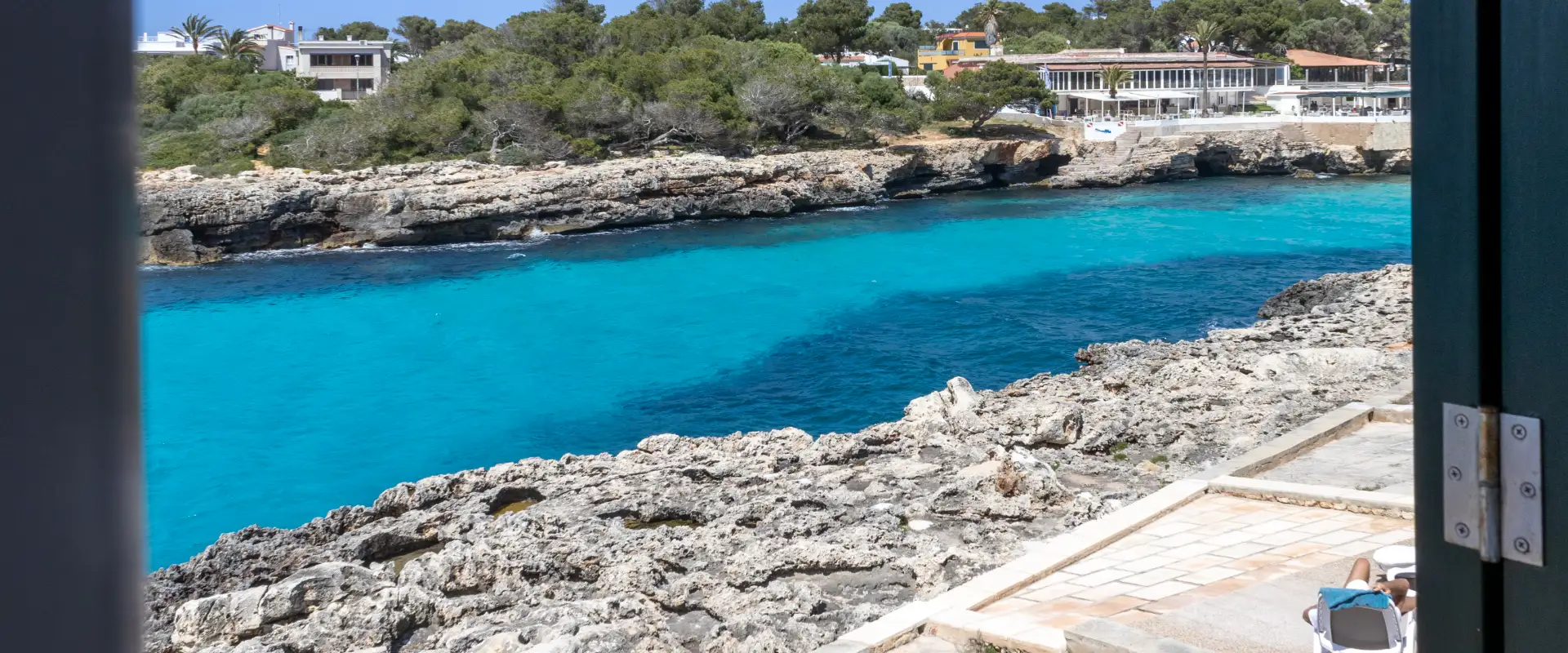 Costa con aguas turquesas y edificaciones rodeadas de vegetaci&oacute;n.