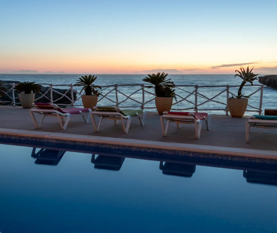 Atardecer junto a una piscina y tumbonas frente al mar.