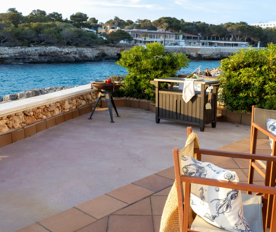 Terraza con vista al mar, muebles, plantas y una parrilla.
